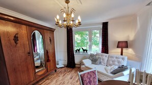 A well-lit room with a wooden floor, a white sofa with patterned cushions, a large mirror, and a chandelier. - Apartment Tilia (Ivenack)
