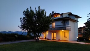 Una casa de dos pisos con balcón, entrada para coches y un árbol en primer plano.