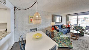Una sala de estar moderna con una pared de ladrillo blanco, una mesa de comedor con sillas, un sofá azul y un sillón estampado.
