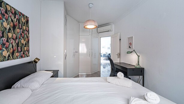 Habitación de hotel con cama, escritorio, silla, lámpara de escritorio, equipo de aire acondicionado y un cuadro en la pared.