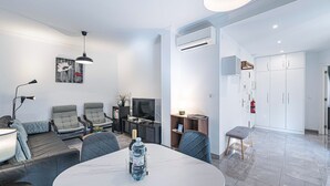 Una sala de estar moderna con una mesa de comedor, sofás grises, un televisor y una botella de agua sobre la mesa.