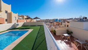 Un área de piscina en la azotea con cielo azul despejado, piscina y mobiliario exterior.
