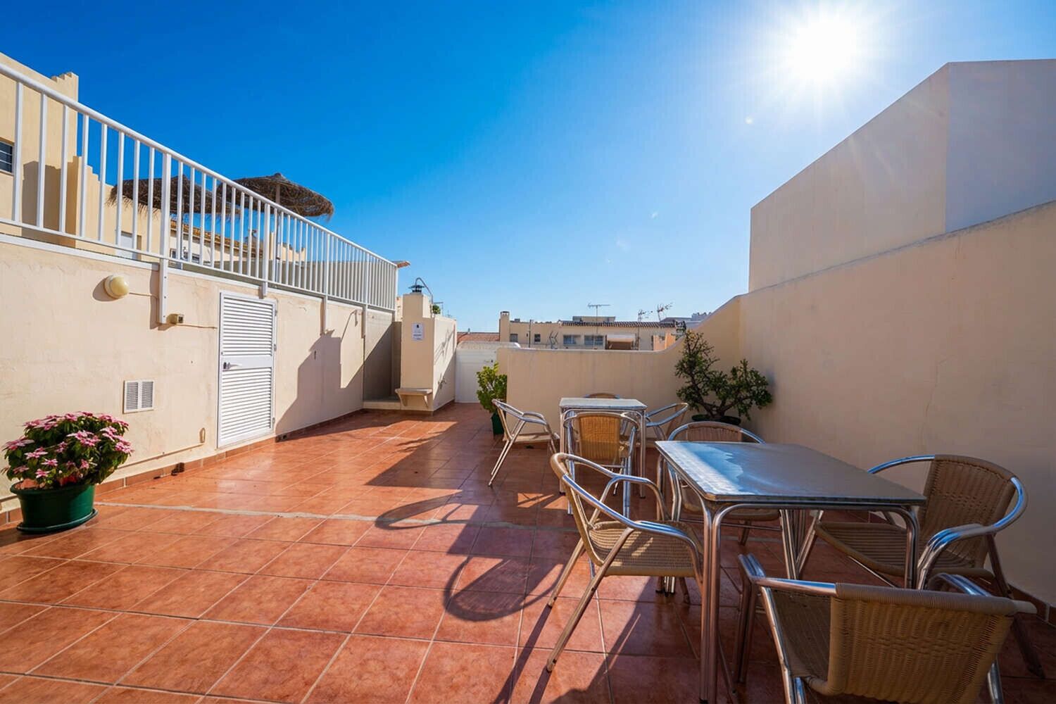 Une terrasse sur le toit, avec une table et des chaises, une rambarde et un pot de fleurs.