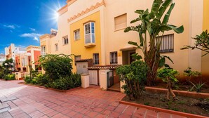 Zona residencial con senderos de tejas de terracota, edificios de color amarillo y blanco, y abundante vegetación, incluyendo plantas de plátano.