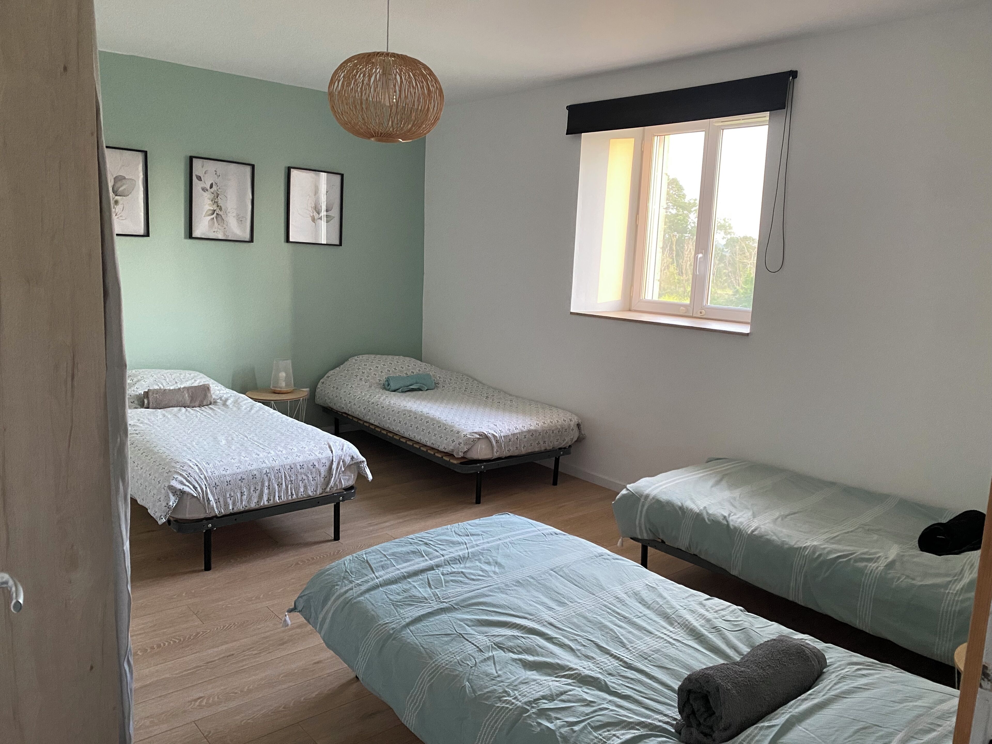 A room with three single beds, a window with a black valance, and three framed pictures on the wall.
