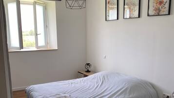 Un dormitorio con una cama grande, una lámpara colgante, un ventanal y tres cuadros con motivos florales en la pared.