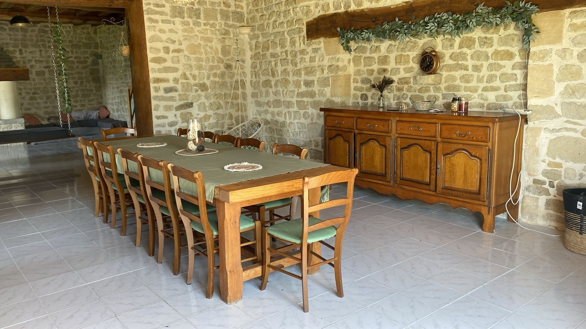 Un coin repas comprenant une longue table et des chaises en bois, un mur en pierre et un meuble en bois doté de tiroirs.