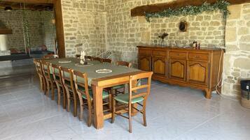 Un coin repas comprenant une longue table et des chaises en bois, un mur en pierre et un meuble en bois doté de tiroirs.