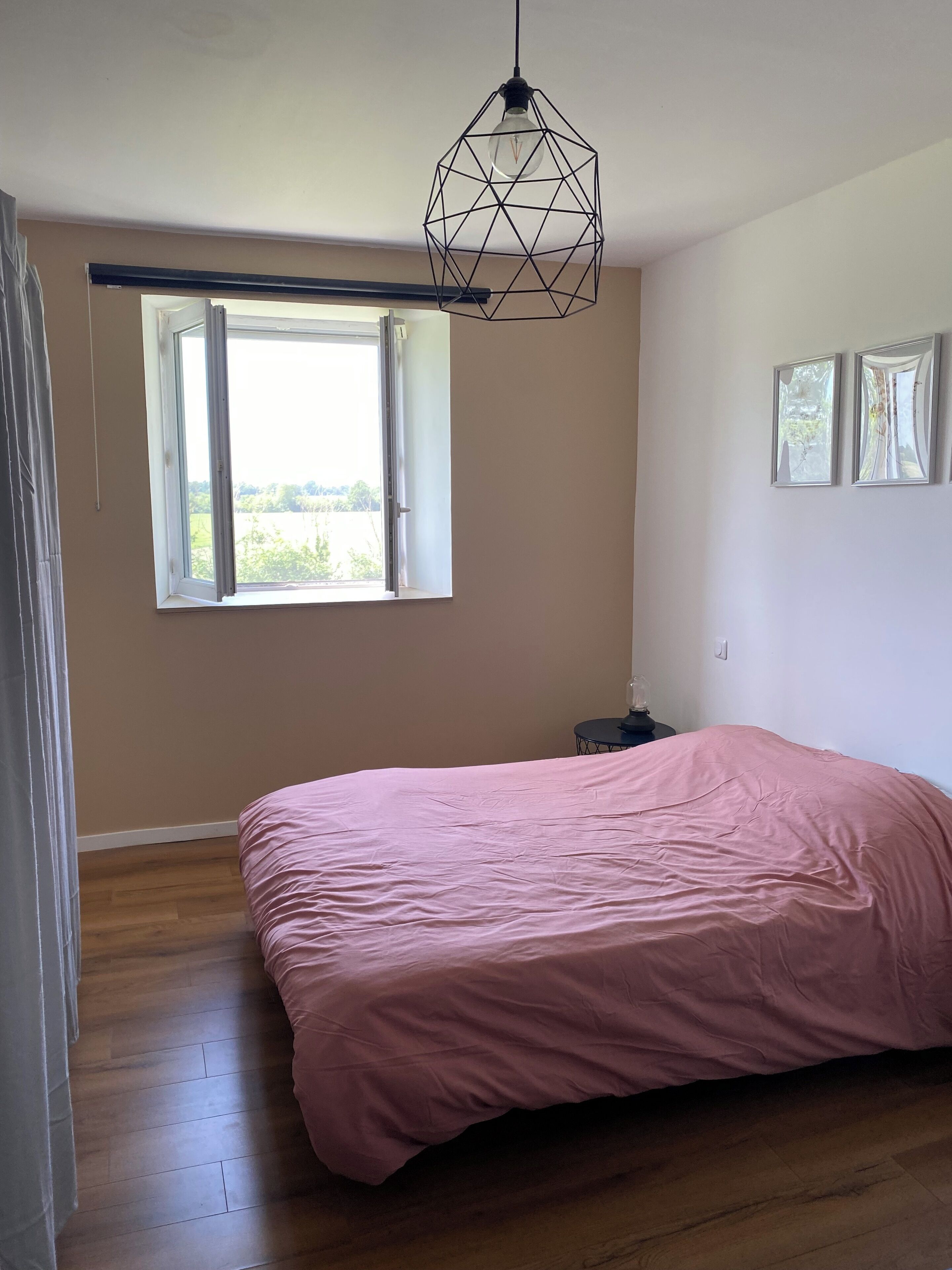 Un dormitorio con una cama grande, una ventana con vistas a follaje y una lámpara con diseño geométrico.