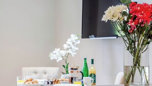 A dining table with breakfast items, a vase with flowers, and a television in the background. - 2 bedroom accommodation in Holt (Holt)