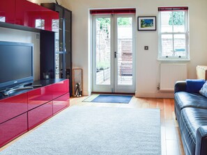 Ein modernes Wohnzimmer mit Flachbildfernseher, roten Schränken, einer schwarzen Ledersofa, Holzboden und einer Schiebeglastür zu einem Außenbereich.