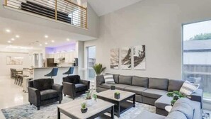 Un amplio salón con un moderno conjunto de sofás, una mesa de centro y un comedor al fondo.