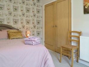 Ein Schlafzimmer mit Bett, Stuhl, Nachttisch mit Lampe und Kleiderschrank.