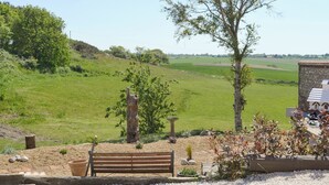 A bench overlooking a grassy field with a stone wall and a tree in the foreground.