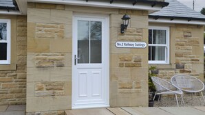 A stone building with a white door, a sign reading 'No.2 Railway Cuttings,' and two white chairs outside.