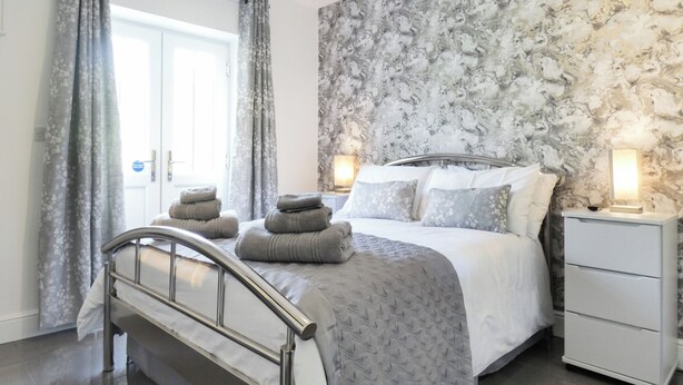 A bedroom with a bed, curtains, a nightstand, and a wall with a marble-like pattern.