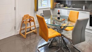 A modern kitchen with white cabinets, a glass dining table, and yellow chairs.