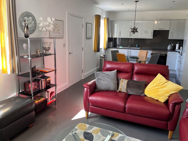 A living room with a red leather sofa, a glass coffee table, and a bookshelf.