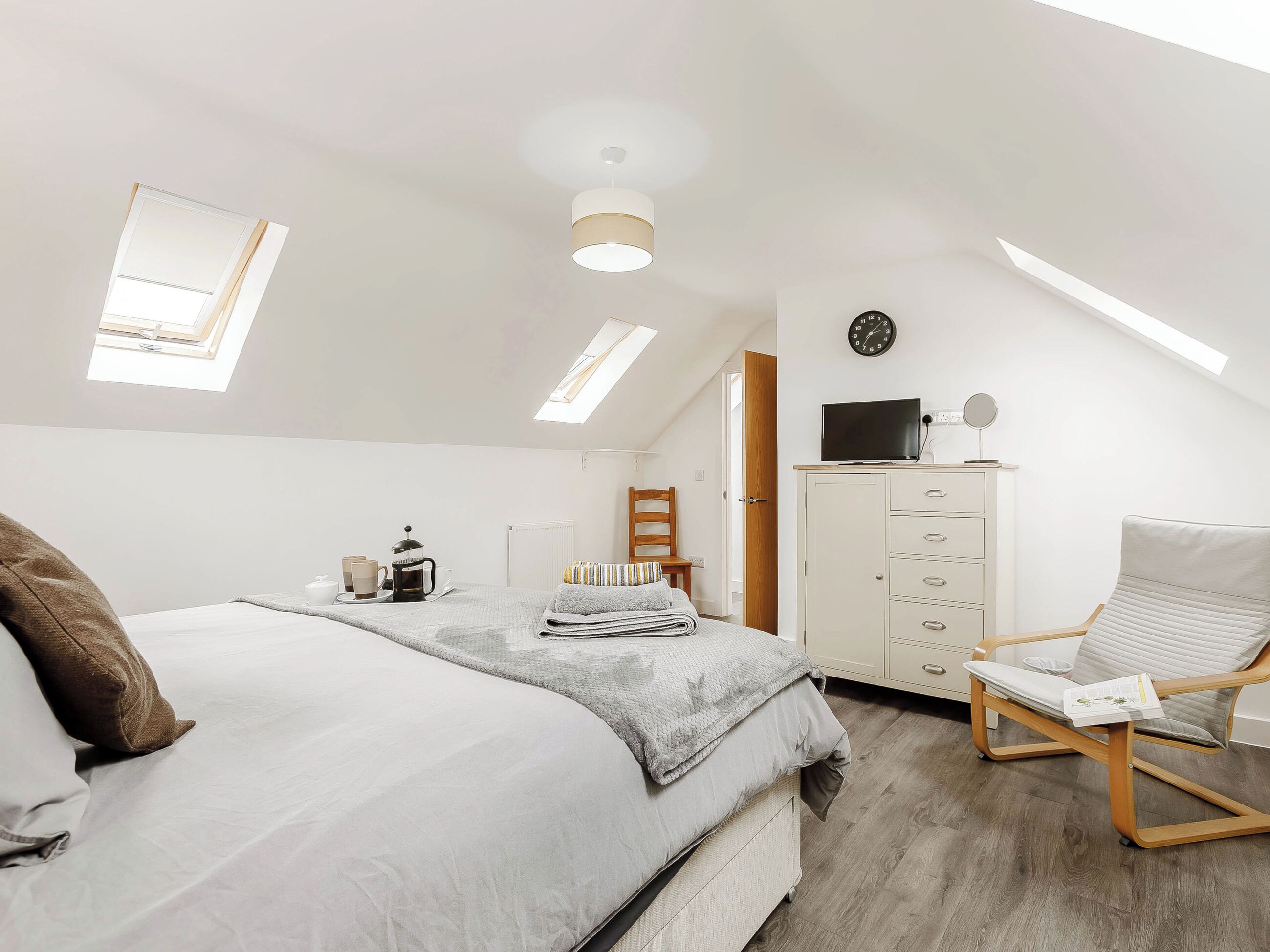 A modern bedroom with a bed, a desk, a chair, a radiator, and a skylight.