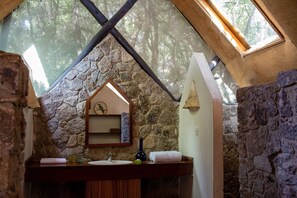 Ein rustikales Badezimmer mit Steinwand, Holzwaschtisch, Spiegel und Dachfenster.