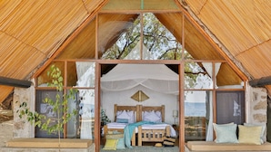A cozy, rustic bedroom with a wooden bed, a window with a view, and a thatched roof structure. - Lukuba Island Lodge (Musoma)