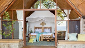 A rustic bedroom with a wooden bed, a canopy, and a view of the sea. - Lukuba Island Lodge (Musoma)