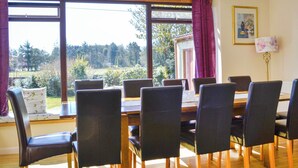 A dining area with a table set for six, large windows with curtains, and a view of a garden.