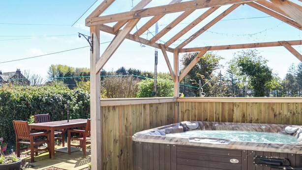 A wooden deck with a hot tub, wooden chairs, and a table.