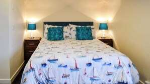 A bedroom with a bed featuring a sailboat pattern, two matching pillows, and two bedside lamps.