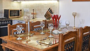 Uma sala de jantar com uma mesa de madeira posta para refeição, um micro-ondas e uma parede de tijolos com armários.