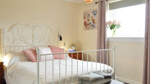 A neatly made bed with a metal headboard, a bedside table with a lamp, and a window with curtains. - 1 bedroom accommodation in Tayport, near St Andrews (Tayport, near St Andrews)