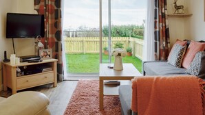 A living room with a TV, sofa, and a view of a backyard. - 1 bedroom accommodation in Tayport, near St Andrews (Tayport, near St Andrews)