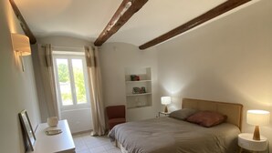 Une chambre à coucher avec un lit, des tables de chevet, un bureau et une fenêtre avec des rideaux.