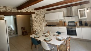 Un coin repas avec une table blanche dressée pour quatre personnes, entouré de murs en pierre et de poutres en bois.