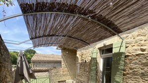 Une terrasse extérieure avec une table et des chaises en bois, une pergola et un mur en pierre.