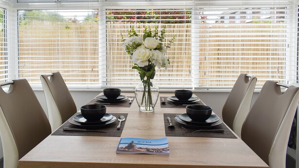 A dining table set for four with black bowls and plates, a vase of white flowers, and a placemat. - 2 bedroom accommodation in Whitstable (Whitstable)