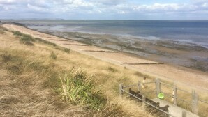 A coastal landscape with a sandy beach, grassy dunes, and a wooden fence. - 2 bedroom accommodation in Whitstable (Whitstable)