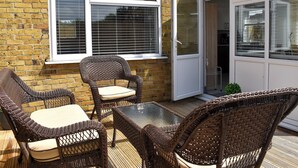 A patio with wicker furniture and a glass table, a brick wall, and a sliding glass door leading to a kitchen area. - 2 bedroom accommodation in Whitstable (Whitstable)