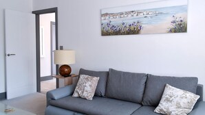 A modern living room with a grey sofa, a painting of a beach scene, and a lamp on a side table. - 2 bedroom accommodation in Whitstable (Whitstable)