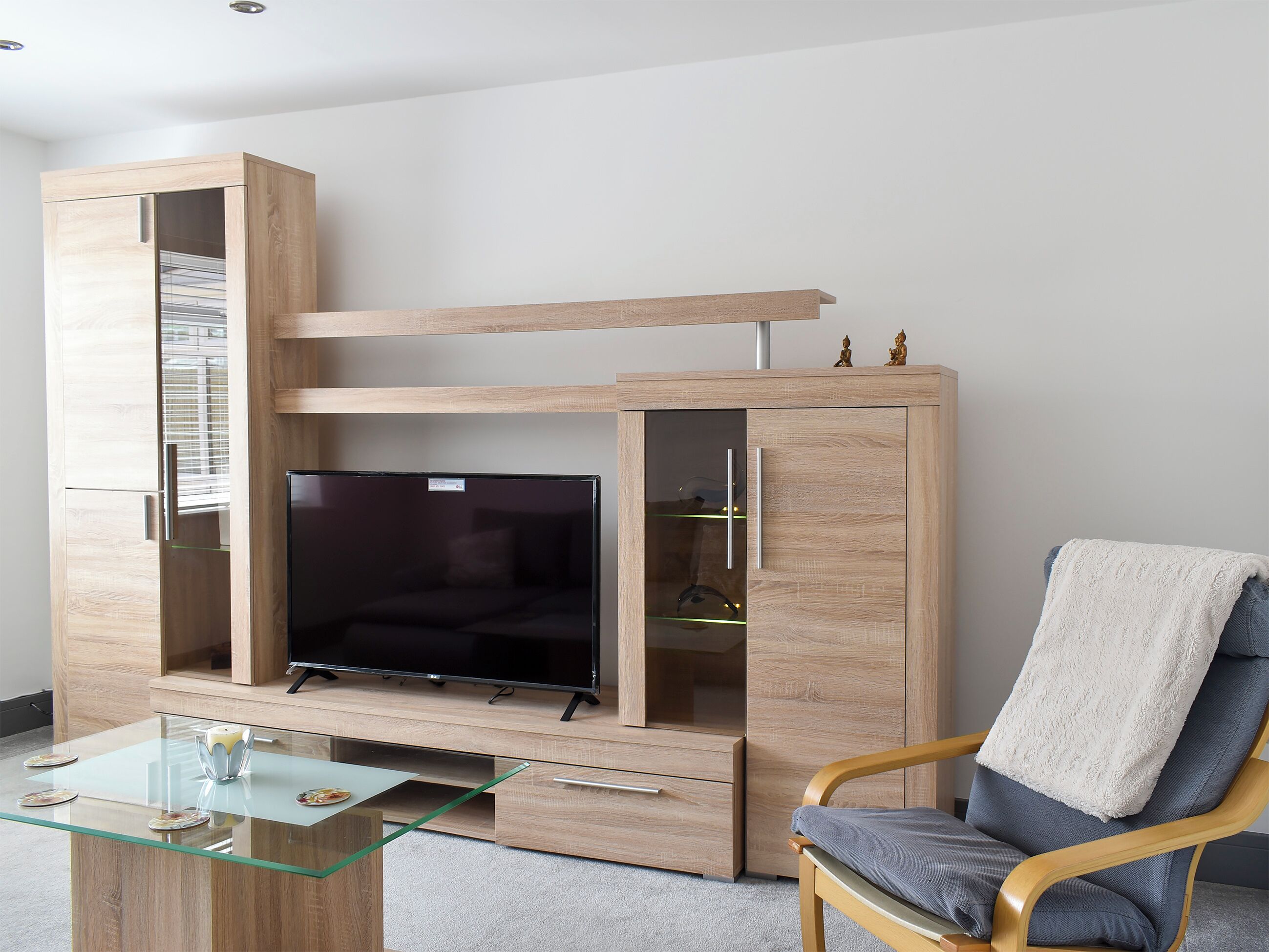 Un soggiorno moderno con TV a incasso, mobiletto in legno, tavolino in vetro e una poltrona comoda.