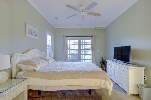 A bedroom with a bed, a dresser, a television, and a ceiling fan.