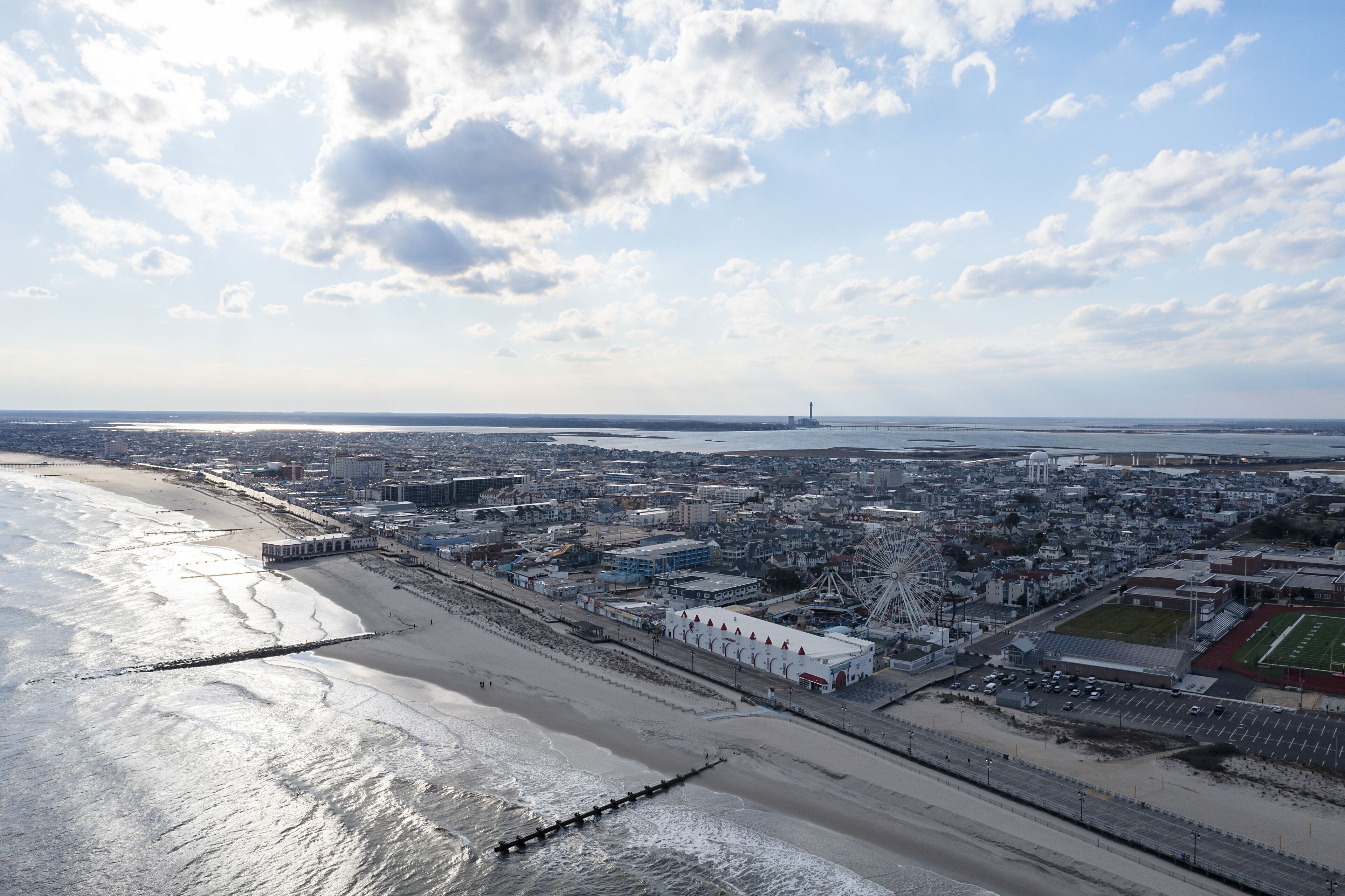 An aerial view of a coastal city with a beach, a pier, and a large Ferris wheel.