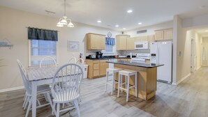 Una cocina moderna con armarios blancos, una isla central con taburetes y un comedor con una mesa y sillas blancas.