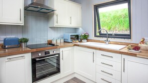Une cuisine moderne avec des meubles blancs, un four encastré, un grille-pain et une fenêtre donnant sur un paysage verdoyant.