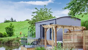 Une cabane moderne dotée d’une terrasse en bois, d’une rambarde en verre et offrant une vue sur un lac.