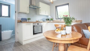 Une cuisine compacte avec des meubles blancs, un four encastré et un coin repas comprenant une table et des chaises en bois.