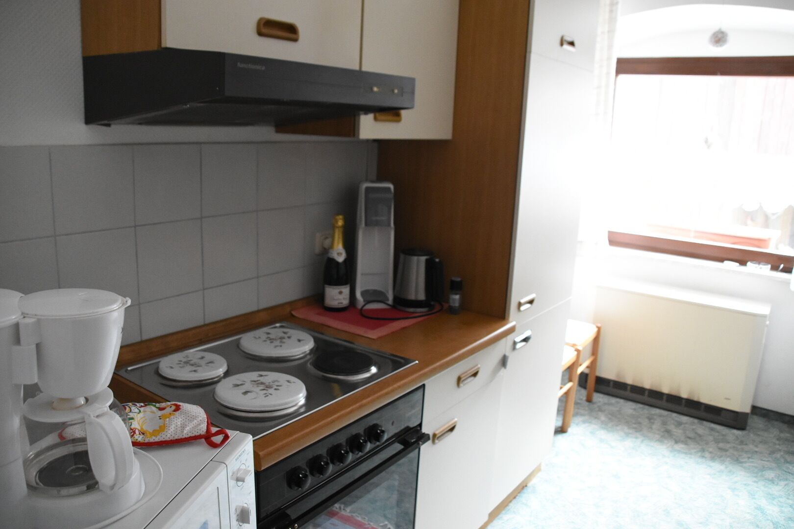 A compact kitchen with a stove, a coffee maker, and a wine bottle on the counter.