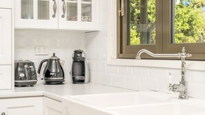 Una cocina con armarios blancos, cafetera, tostadora y ventana con vista a árboles.