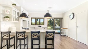 Una cocina moderna con una isla central, taburetes de bar, iluminación colgante y vistas al exterior.