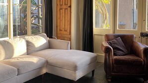 A living room with a beige sectional sofa, a brown leather armchair, and a wooden door. - Southfield Art Studio (Braunston, near Daventry)